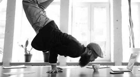 Bearded man doing hand stand on desk