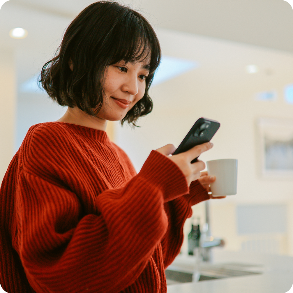 Woman looking at her phone holding a coffee mug.